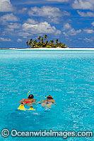 Snorkel divers exploring crystal clear lagoon water surrounding a tropical coconut palm fringed island. Cocos (Keeling) Islands, Indian Ocean, Australia