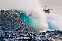 A helicopter filming a tow-in surfer at Peahi (Jaws) off Maui. Hawaii. The person in the foreground is driving a jet ski.
