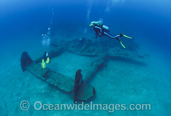Scuba divers observing a Lockheed P-38 Lightning World War II American fighter aircraft, resting intact on the sea floor in Milne Bay, Papua New Guinea. Within the Coral Triangle. Photo - Bob Halstead