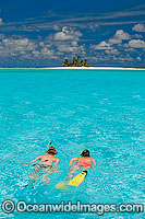 Snorkel divers exploring crystal clear lagoon water surrounding a tropical coconut palm fringed island. Cocos (Keeling) Islands, Indian Ocean, Australia